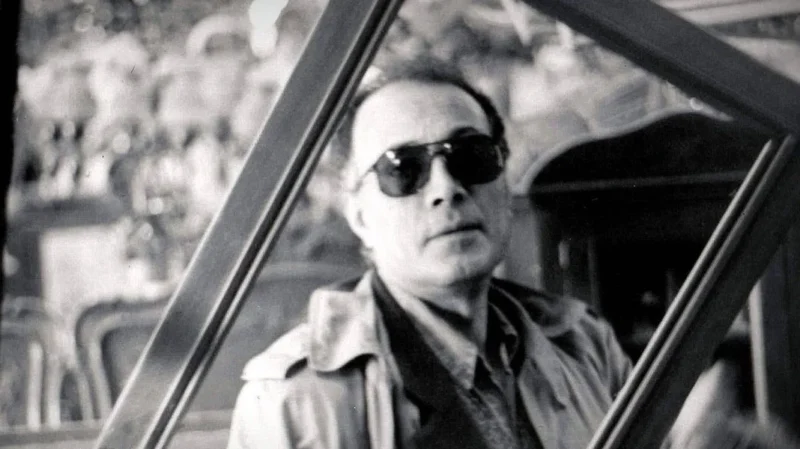 Abbas Kiarostami, wearing glasses, gazes through a hollow windowpane.