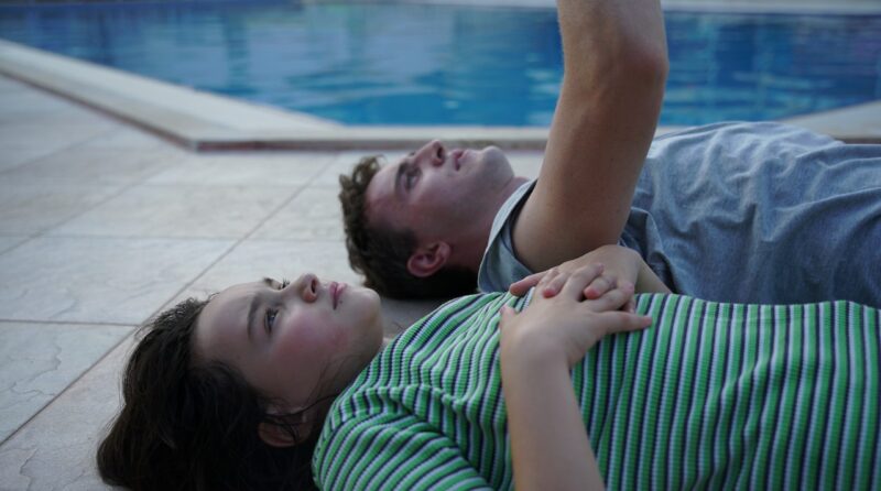 A father and daughter lying down by a pool, gazing at the sky.