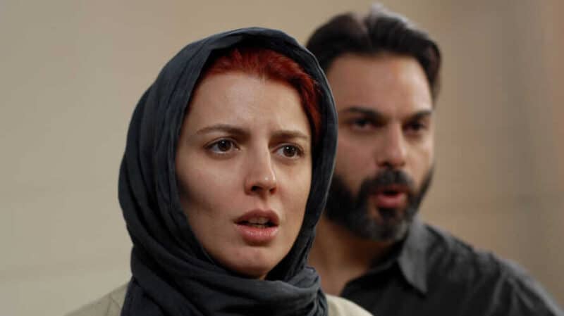 Leila Hatami as Simin in the movie "Jodaeiye Nader az Simin" appears worried at the forefront. Peyman Moadi as Nader stands slightly nervous behind her.