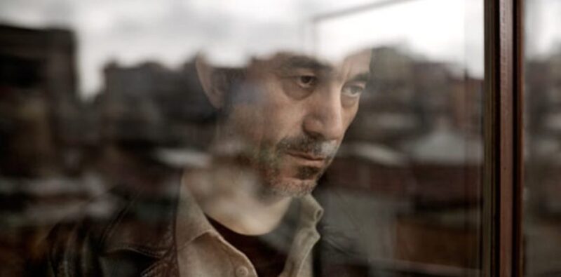 Nuri Bilge Ceylan, portraying a character, gazing out of a window with a somber expression.