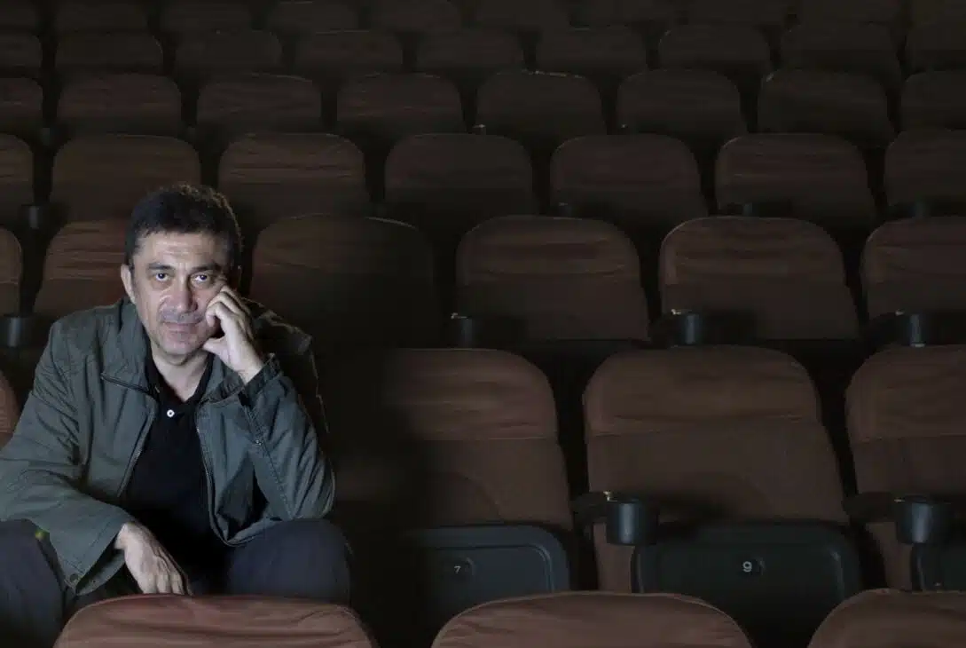 Nuri Bilge Ceylan, a film director, gazing at the camera in a movie theater while resting his hand on his chin.