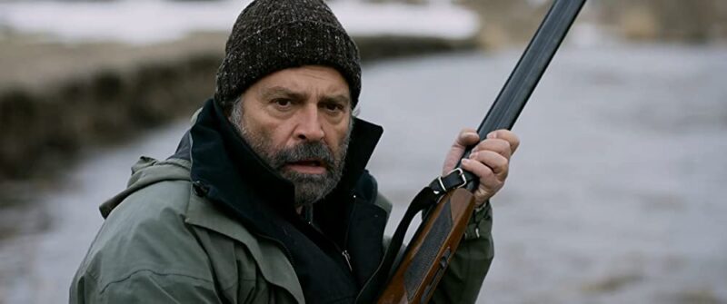 Aydin (Haluk Bilginer) holding a gun while hunting, with a horrified expression.