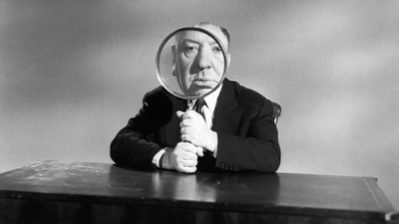 Alfred Hitchcock holding a magnifying glass to his face.