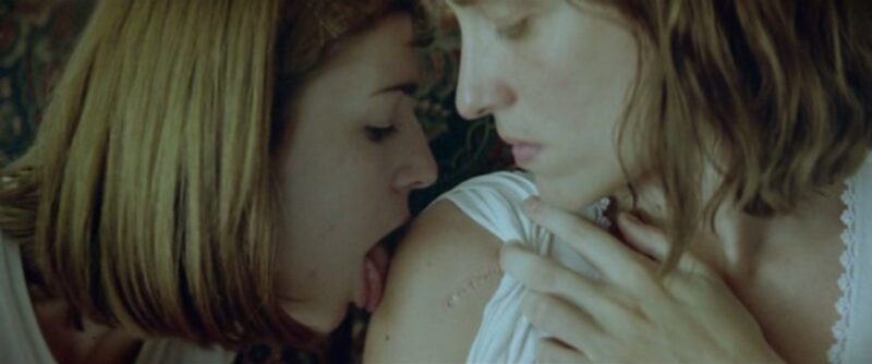 Aggeliki Papoulia and Mary Tsoni as the two sisters from the movie Dogtooth. One sister licks the shoulder of the other.