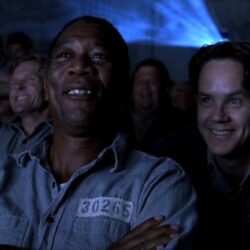 A still from the movie "The Shawshank Redemption," depicting a group of inmates gathered together in the prison yard, watching a movie projected onto a sheet.