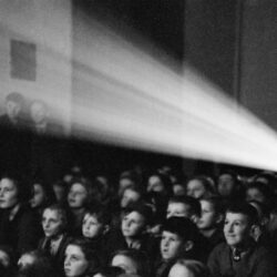 Children watching a movie reflected on a white screen in a movie theater.