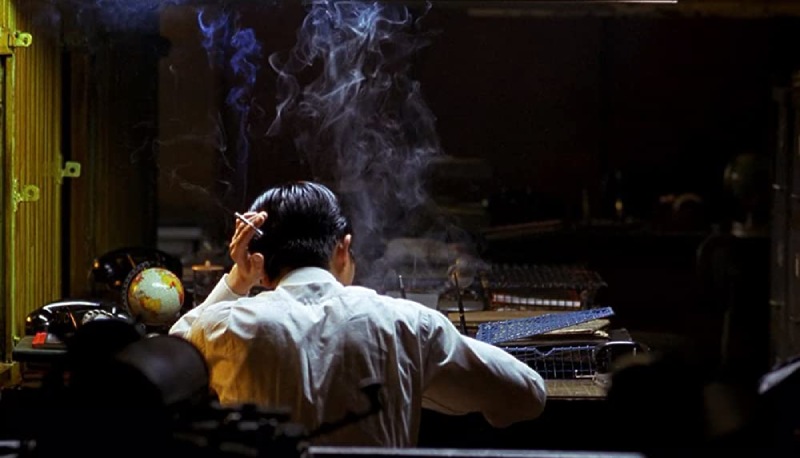 Chow stands with his back turned in this still from "In The Mood For Love", surrounded by cigarette smoke, creating a melancholic ambiance.