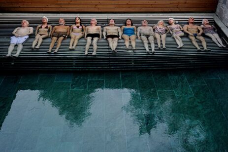 Group of people sunbathing on their backs by the pool, lined up side by side in a bird's eye view.