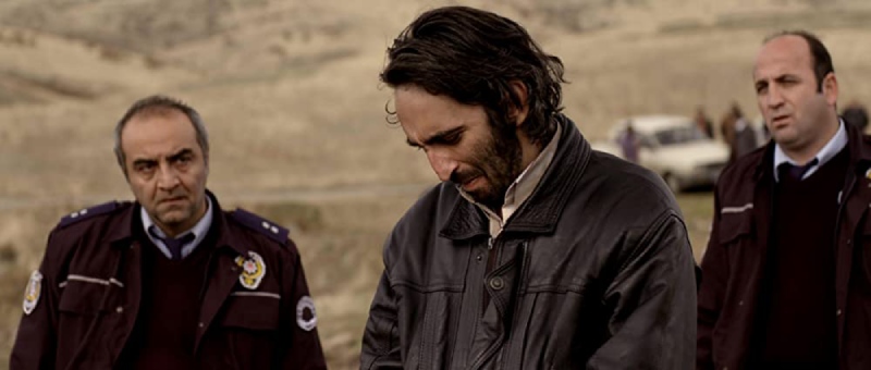 A frame from Once Upon a Time in Anatolia showing Suspect Kenan, Commissar Naci, and Police Officer Izzet in the same shot. Kenan looks down with guilt.
