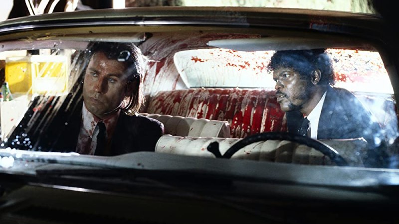Image of Vincent Vega (John Travolta) and Jules Winnfield (Samuel L. Jackson) sitting in a car, startled by an exploding gun, from the movie Pulp Fiction.