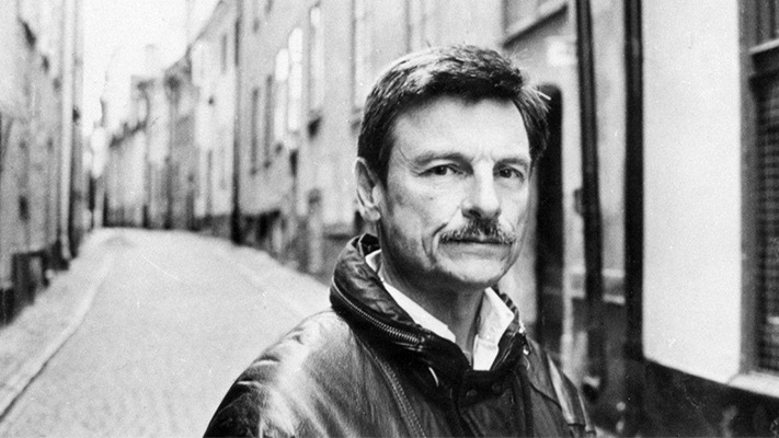 Andrei Tarkovsky, with an intense gaze, looks directly at the camera against the backdrop of a bustling street.