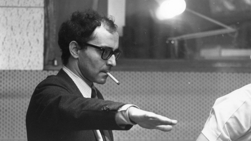 Renowned filmmaker Jean-Luc Godard with a cigarette in his mouth, directing the film production team.