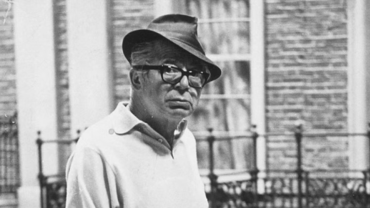 Billy Wilder, wearing a stylish fedora, gazes thoughtfully with a contemplative expression.