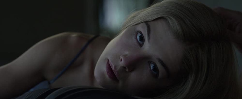 Rosamund Pike as Amy Dunne in Gone Girl, lying face-down on the bed with a menacing upward gaze in the final scene.