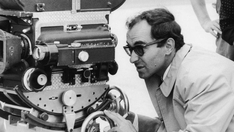 Jean-Luc Godard examining the movie set through the viewfinder of a camera.