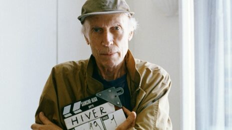 Eric Rohmer, a renowned filmmaker, standing confidently while holding a clapperboard.