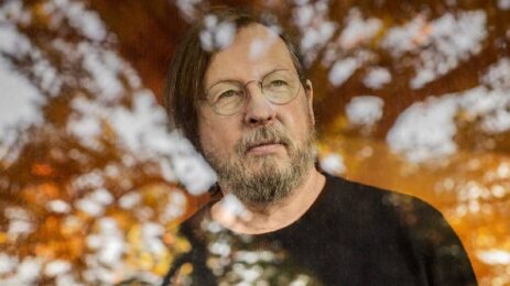 Lars von Trier wearing glasses, deep in thought while gazing through the glass.