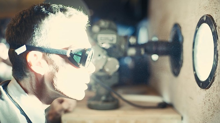 J. Robert Oppenheimer (portrayed by Cillian Murphy) wearing goggles, observing the brilliant, powerful glow of the atomic bomb during testing in the movie Oppenheimer.