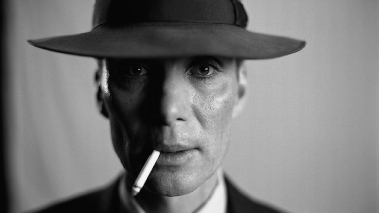 J. Robert Oppenheimer (portrayed by Cillian Murphy) wearing a hat and holding a cigarette in mouth, gazing pensively ahead in the movie Oppenheimer.