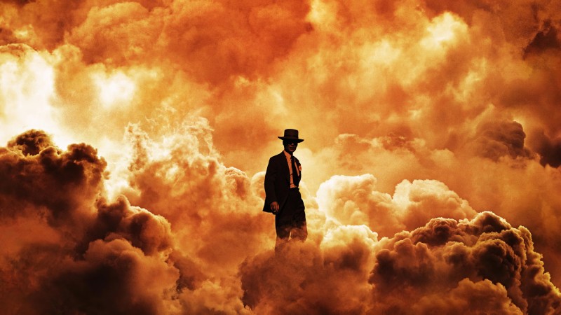 J. Robert Oppenheimer (played by Cillian Murphy) standing amidst the fiery aftermath of an atomic bomb explosion. Movie poster for Oppenheimer.