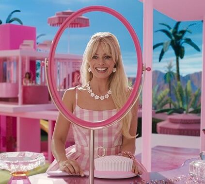 Margot Robbie as Barbie smiling at her reflection in an empty mirror in a scene from the movie.