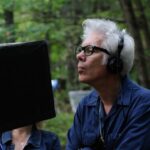 10 Signature Elements of Jim Jarmusch's Filmmaking Style! Jim Jarmusch, the director, focuses intently on his movie's progress as he observes the monitor in front of him.