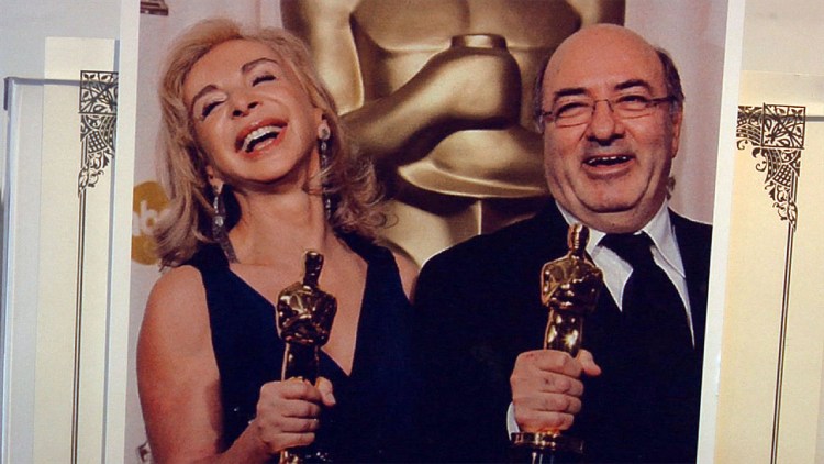 Dante Ferretti and his wife Francesca Lo Schiavo wear joyful smiles as they hold the Oscar trophy in their hands.