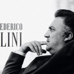10 Signature Elements of Federico Fellini's Filmmaking Style! Federico Fellini leans back in his chair, hand to his mouth, with the caption 'Directed by Federico Fellini' visible in the photo.