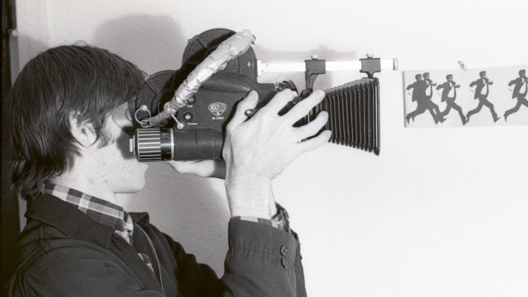 Gus Van Sant peers through his camera's side-angle viewfinder, focusing on capturing the perfect shot.
