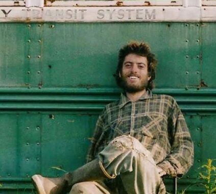 Christopher McCandless, seated with legs crossed against his iconic trailer, laughs with a sense of accomplishment and relief, having established a sense of order in his life.