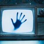 A chilling scene with a weathered television featuring a mysterious hand, setting the stage for a spine-tingling horror movie.