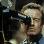 10 Signature Elements of Ridley Scott's Filmmaking Style! Director Ridley Scott peers through the camera's viewfinder, actively engaged in directing a movie.