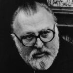 10 Signature Elements of Sergio Leone's Filmmaking Style! Director Sergio Leone, wearing glasses, looks downwards with a focused expression.