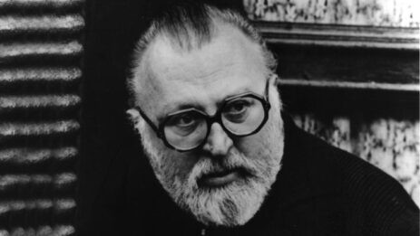 Director Sergio Leone, wearing glasses, looks downwards with a focused expression.
