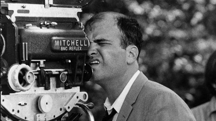 Terrence Malick directing on set, framing a shot through the viewfinder of a Mitchell brand camera.
