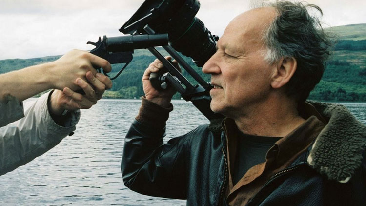 Werner Herzog, camera in hand, gazes at a person holding a gun.