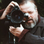 10 Signature Elements of Orson Welles's Filmmaking Style! Orson Welles, with a focused expression, looks through the camera viewfinder while directing a film scene.