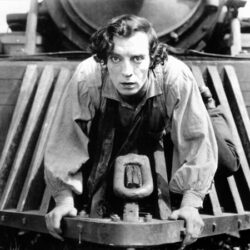 10 Signature Elements of Buster Keaton’s Filmmaking Style! Buster Keaton embarks on an exhilarating journey, clinging to the front of a moving train in a daring and thrilling scene.