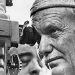 10 Signature Elements of Sam Peckinpah’s Filmmaking Style! Close-up shot of director Sam Peckinpah looking through the camera's viewfinder, engaged in directing the film.