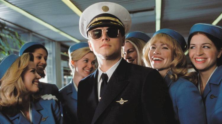 Scene from the movie 'Catch Me If You Can' featuring Frank Abagnale (Leonardo DiCaprio) on stage with women behind him.