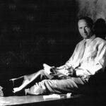 10 Signature Elements of Michael Curtiz’s Filmmaking Style Michael Curtiz lying on a table, holding a notebook and pen, making notes while looking toward the camera.