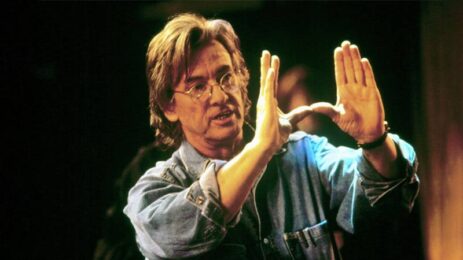 Paul Verhoeven on a film set, directing a scene by gesturing with his hand to indicate the movie's scene.