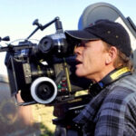 10 Signature Elements of Ron Howard’s Filmmaking Style! Ron Howard on a film set, peering through a camera viewfinder with a focused expression while directing a movie.