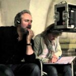 10 Signature Elements of Sam Mendes’s Filmmaking Style! Sam Mendes in front of a monitor with headphones on, on a movie set, intensely focused on the scene being filmed.