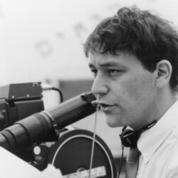 Sam Raimi beside the movie camera on set, focused on directing while holding a script.