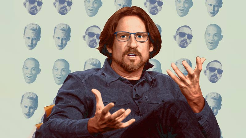10 Signature Elements of David Ayer's Filmmaking Style! 1 Director David Ayer seated, opening his hands in thought, with heads of characters from the films he directed behind him.