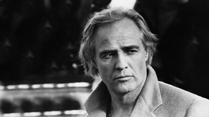 Marlon Brando wearing a coat, glancing to his left, striking a charismatic pose.
