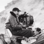 10 Signature Elements of Bernardo Bertolucci's Filmmaking Style! Director Bernardo Bertolucci in the director's chair, behind the camera, laughing and visibly enjoying the stage.