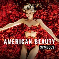 What "American Beauty" Symbols Really Mean? — Plastic Bag, Roses, and More! Mena Suvari as Angela Hayes lying among roses in the iconic bird's eye view shot from the movie American Beauty. Text overlay reads 'American Beauty symbols.